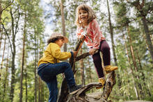 Kaksi lasta kiipeilee puun juurakon päällä metsässä.