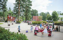 Kesäpäivä Myllynsiiven leikkipuistossa. Lapsia juoksee pihalla. Lapsia pienen karusellin kyydissä.