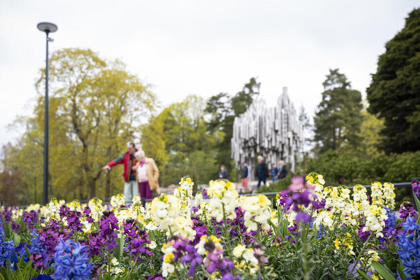 Etualalla värikkäitä kukkia ja takana puita sekä Sibelius-monumentti.