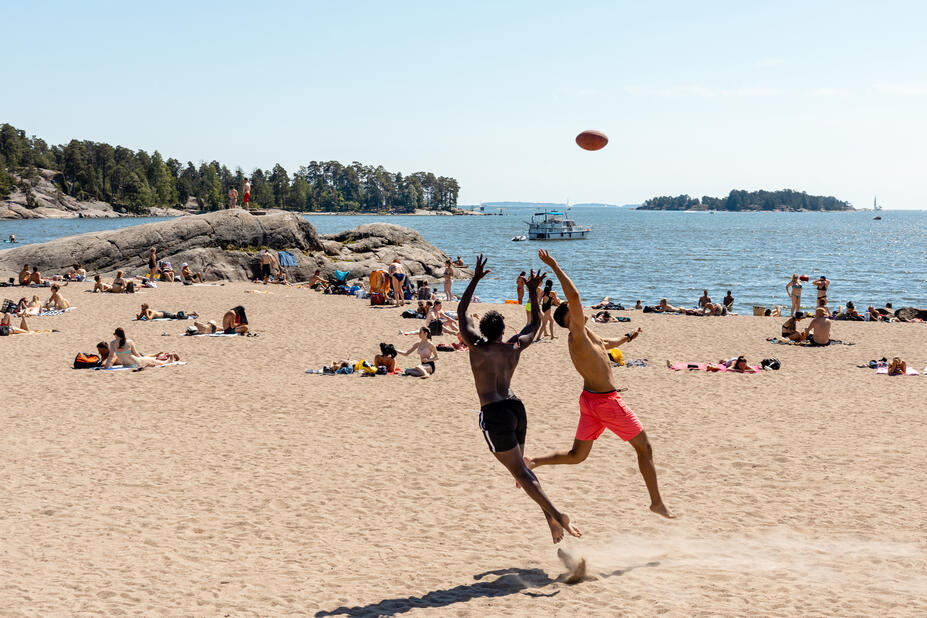 Uimarannalla oleskelee useita ihmisiä, kaksi henkilöä heittelee palloa.