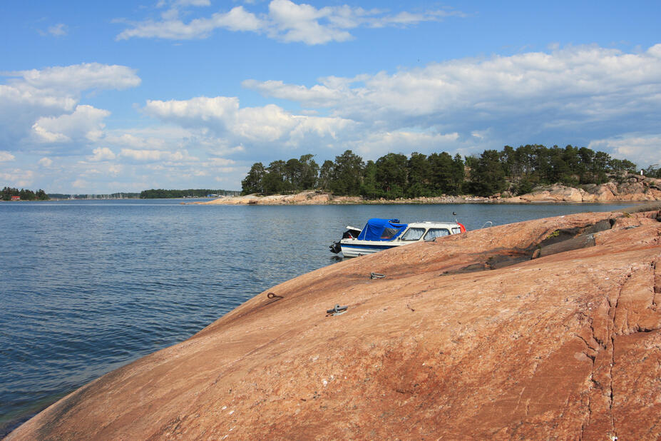 Rantakallion takaa pilkottaa rantautunut vene.