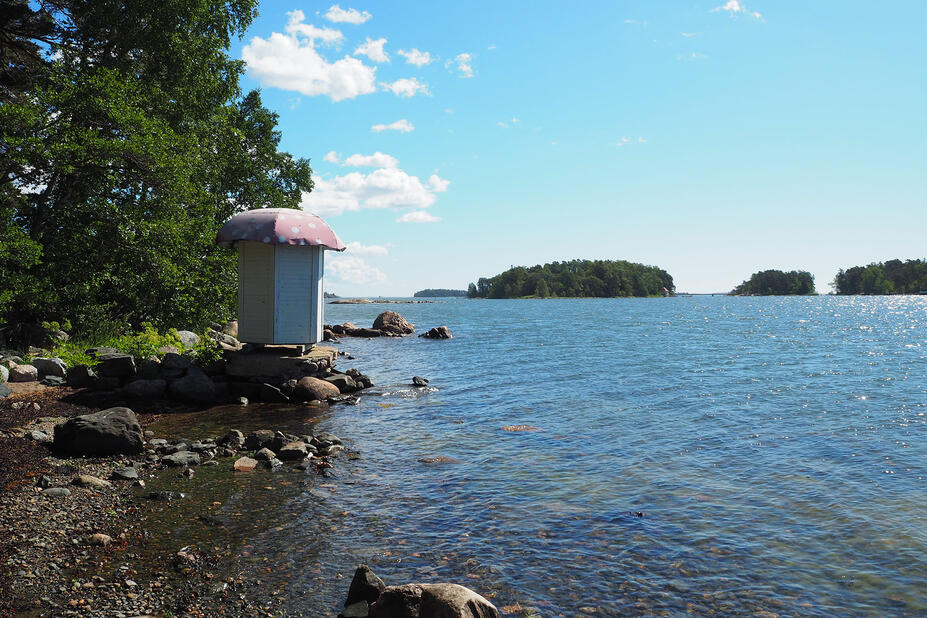 Kivisellä rannalla uimakoppi, meri ja puita.