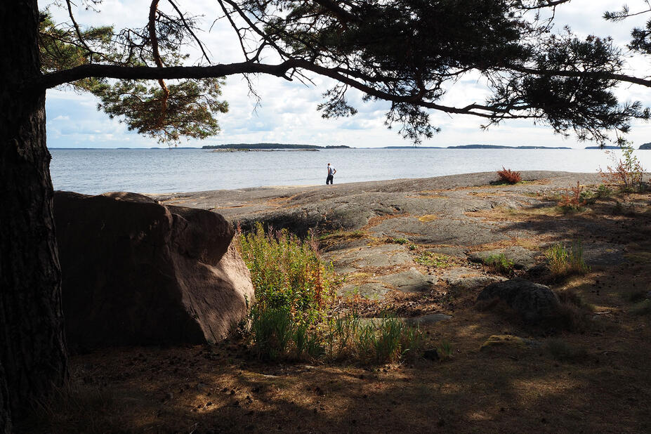 Henkilö kävelee kallioisella rannalla meren tuntumassa.