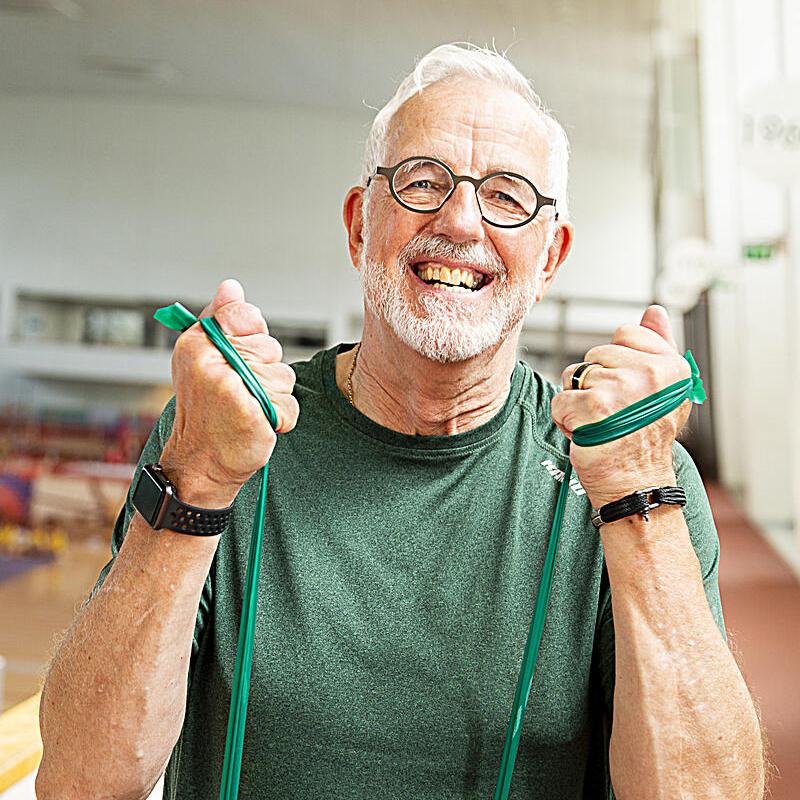 An elderly man is happily exercising using a resistance band.