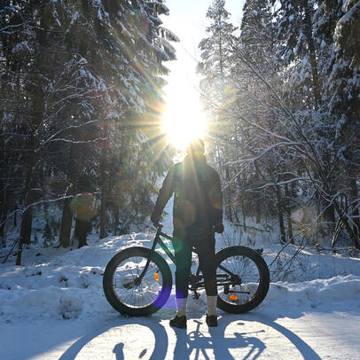 Henkilö seisoo vastavalossa talvisella tiellä pyörän kanssa.