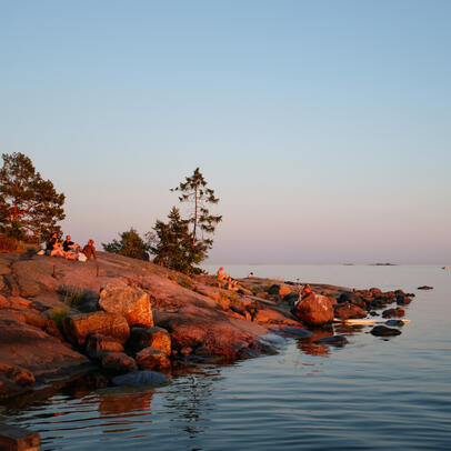 Henkilöitä rantakalliolla ilta-auringossa.