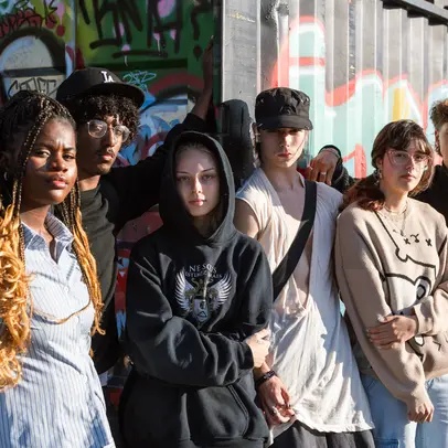 A group of young people standing in front of a graffiti wall.