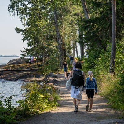 Kävelijöitä rantatiellä, puita ja meri.