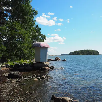 Kivisellä rannalla uimakoppi, meri ja puita.