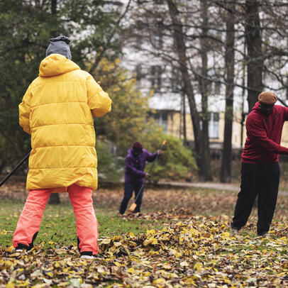 Three people raking leaves in a park.