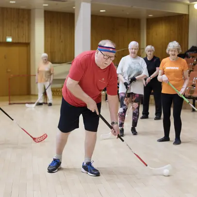 Five older people playing floorball in a sports hall.