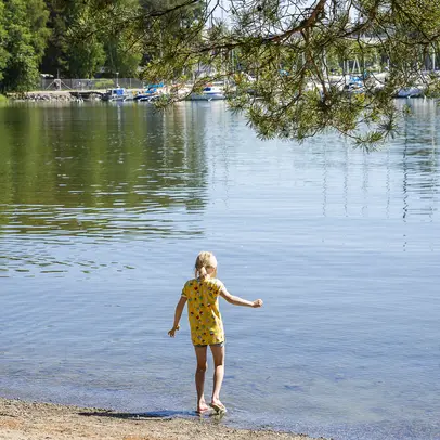 Lapsi kävelle hiekkarannan rantaviivan tuntumassa kohti vettä.