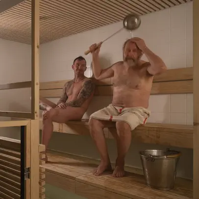 Kaksi ihmistä saunoo Yrjönkadun uimahallin puusaunassa. Toinen kaataa kauhalla vettä päänsä ylle.