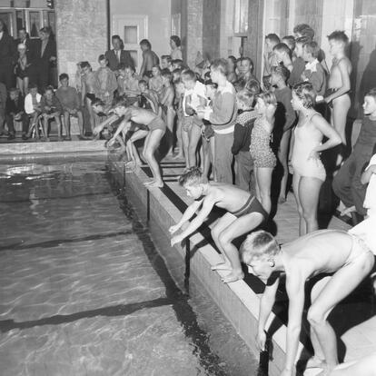 Nuoria uimareita hyppäämässä altaaseen mustavalkoisessa kuvassa.