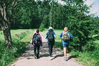 Kolme henkilöä kävelemässä reput selässä hiekkatiellä.