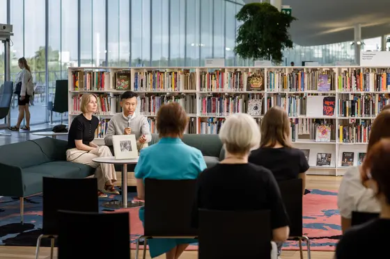 En författare och en intervjuare sitter i en soffa på centrumbiblioteket Ode och samtalar i en mikrofon inför publiken.