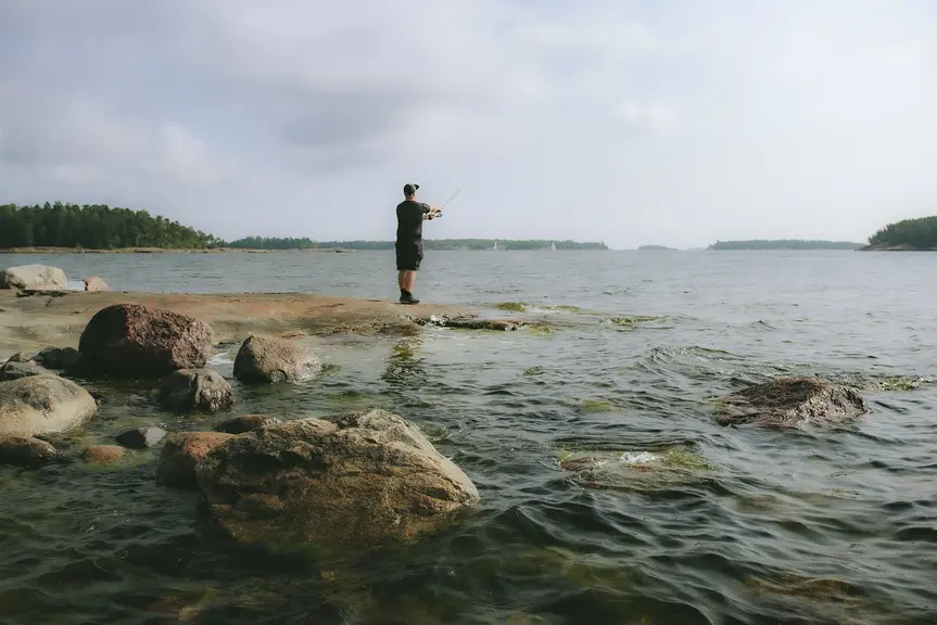 Kalastaja vavan kanssa kallion päällä meren äärellä.