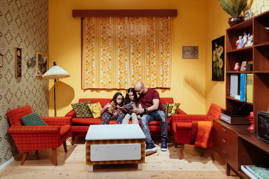 A man is reading a newspaper with two children in a retro-style room