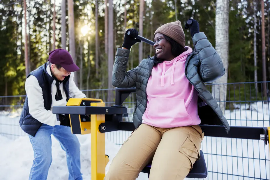 A younger and an older woman are working out at an outdoor gym in winter.