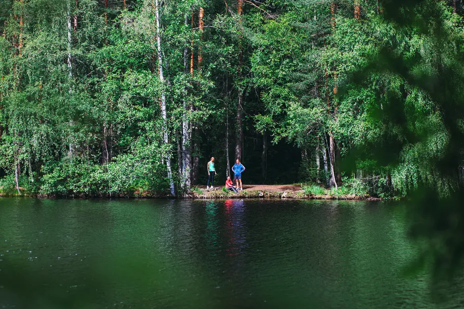 Tre personer i utkanten av skogen invid ett vattendrag.