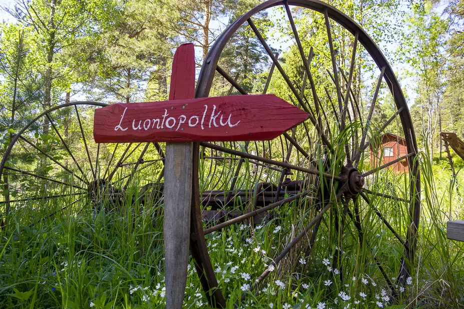 Punainen luontopolun kyltti vanhaa rattaan rautaista rengasta vasten.