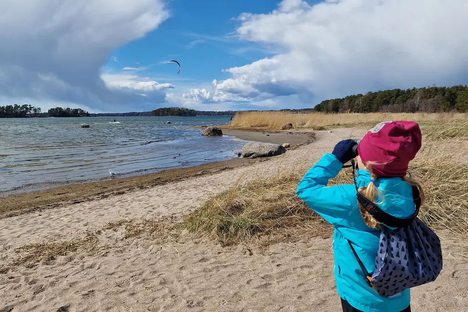 Lapsi kiikaroi hiekkarannalla merelle