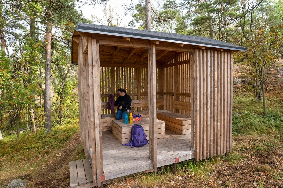 Nainen kaivaa eväitä repusta katoksellisessa taukomajassa