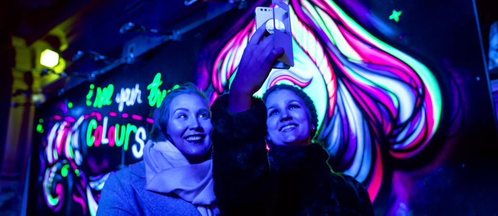 Lux Helsinki 2018. Talvinen ilta. Naiset ottamassa selfie-kuvaa fluorisoivan taiteen äärellä.