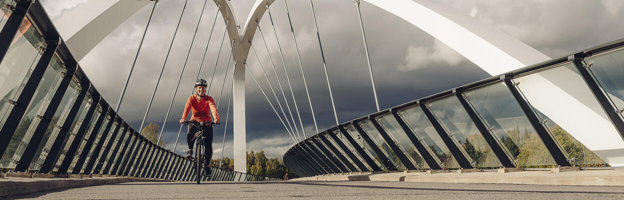 A woman rides a bike on the Aurora bridge wearing an orange shirt.