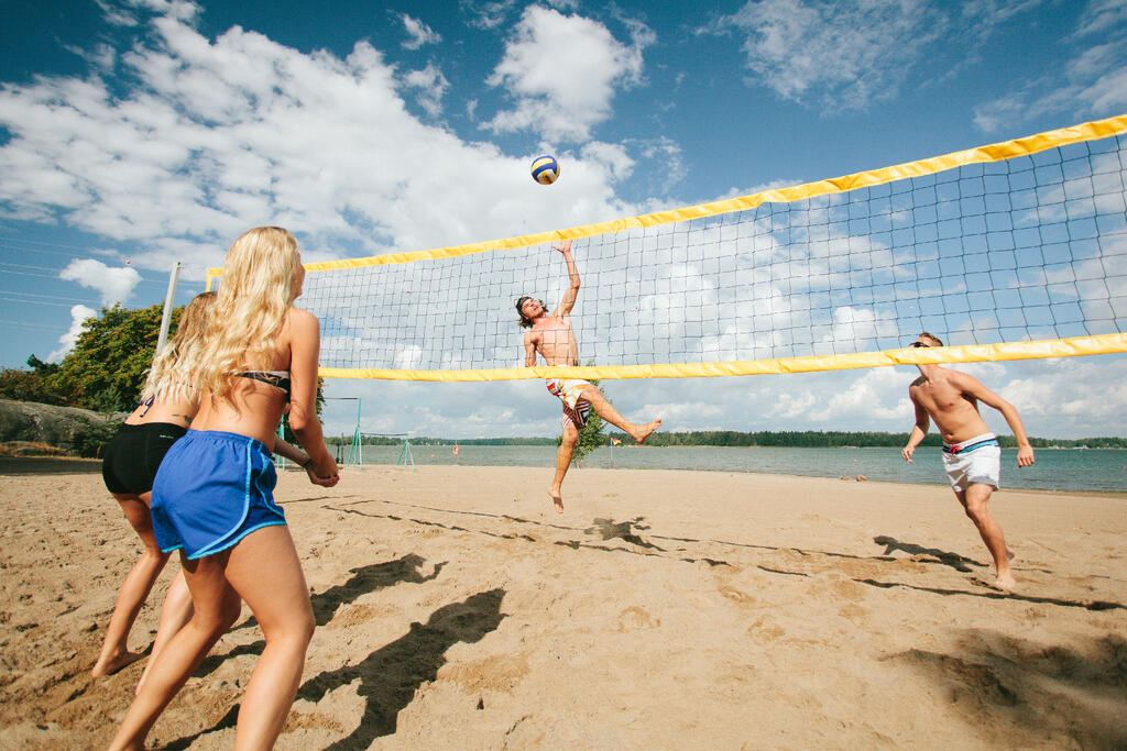 Neljä henkilöä pelaa rantalentopalloa hiekkarannalla.