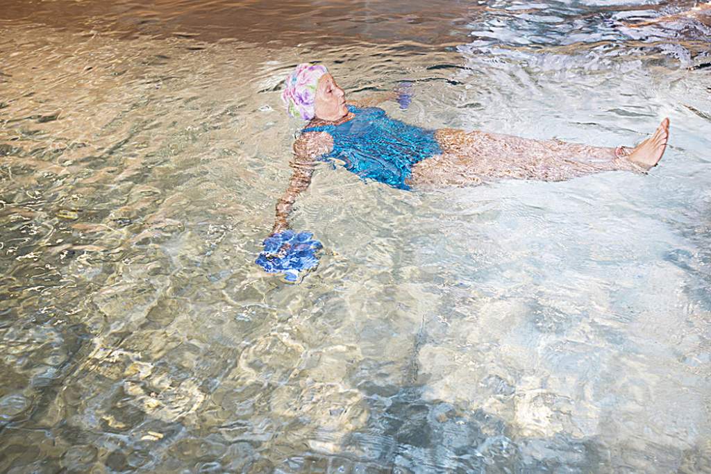 En äldre kvinna flyter på rygg i en simbassäng med hjälp av simdynor.