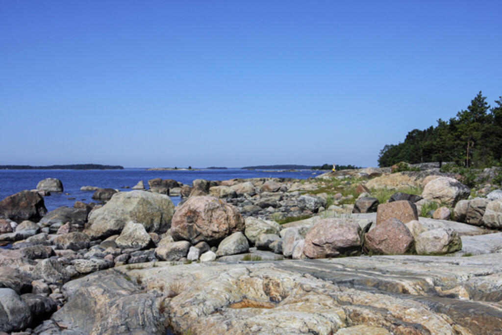 Kaunissaaren kivikkoista rantaa ja sinitaivas.