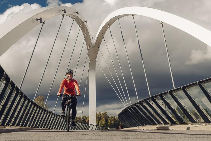 A woman rides a bike on the Aurora bridge wearing an orange shirt.