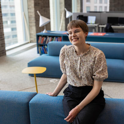 Nainen nojaa toimiston sohvaan ja hymyilee