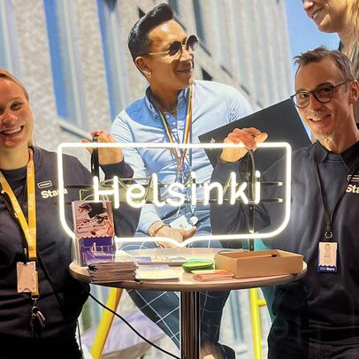 Kaksi kaupungin työntekijää poseeraa Helsinki-kyltin vieressä.