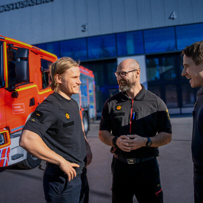 Kolme miestä paloaseman pihalla.