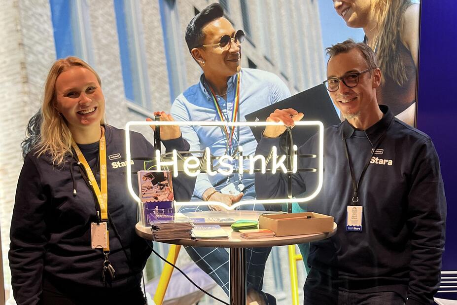 Kaksi kaupungin työntekijää poseeraa Helsinki-kyltin vieressä.