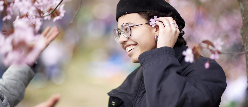 Hymyilevä nainen asettaa kirsikankukkaa silmälasien kehykseen.