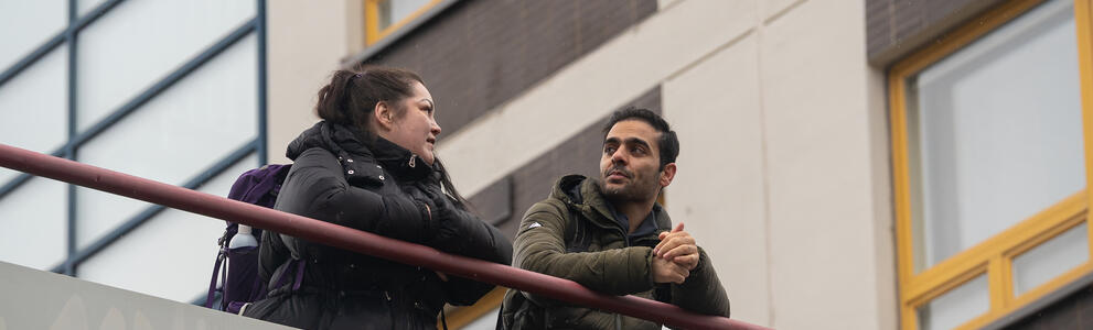 Nainen ja mies nojaavat kaiteeseen ja keskustelevat