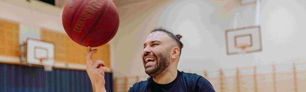 Liikuntacoach pyörittää koripalloa sormensa päällä Helsingin liikuntasalissa.