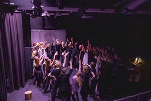 30 näyttelijää lavalla piirissä oikea käsi kohti taivasta