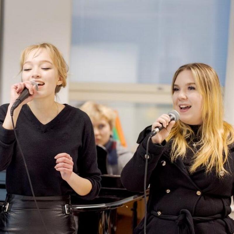 Kuvassa on kaksi opiskelijaa laulamassa mikrofoneihin.