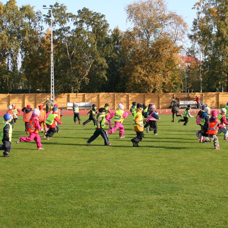 Lapsia huomioliivit päällä juoksemassa urheilukentällä