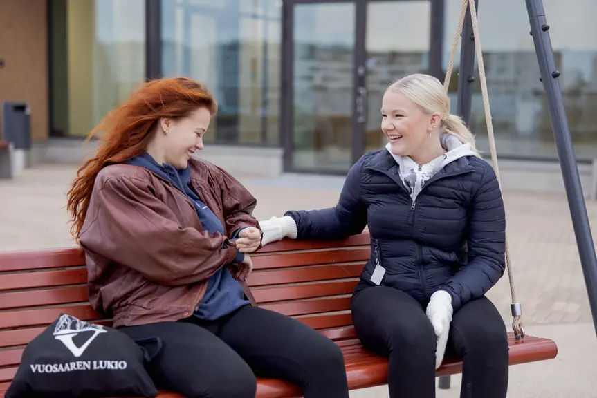 Kaksi opiskelijatyttöä istumassa koulun pihalla