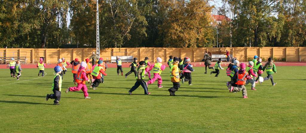 Lapsia huomioliivit päällä juoksemassa urheilukentällä