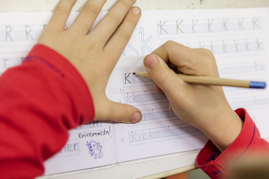 Lapsen kädet kirjoittaa K-kirjaimia kirjoitusvihkoon