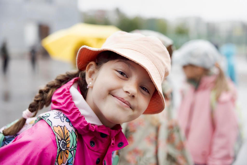 Lapsi hymyilee kameralle koulun pihalla sateisena päivänä.