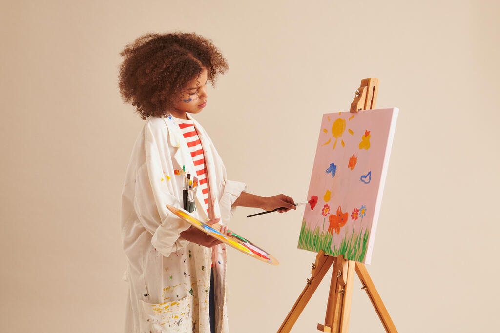 Lapsi maalaa taulua iso taiteilijatakki päällään
