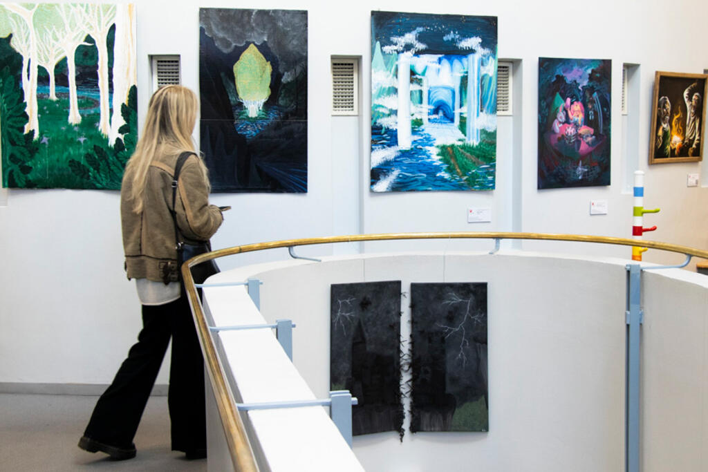 Opiskelija tarkastelee maalauksia Kallion kirjaston lukiodiplominäyttelyssä. Kuva: Loviisa Kangas