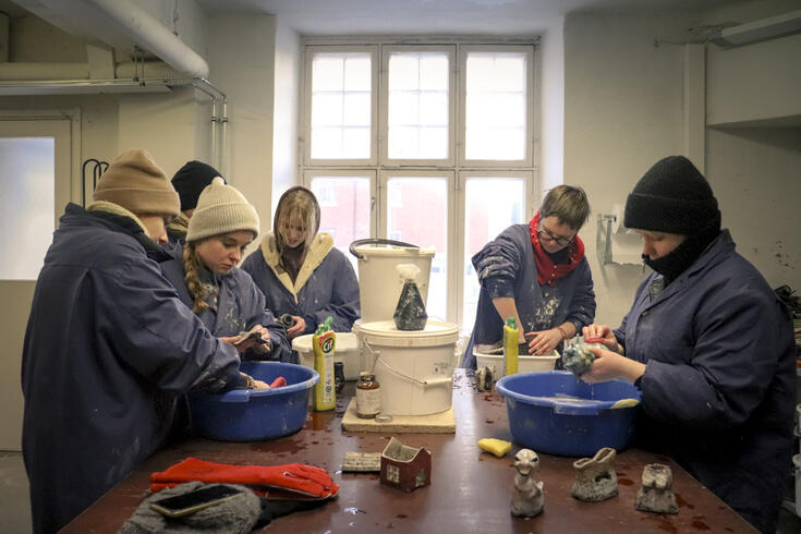 Opiskelijat tekevät rakukeramiikka yhteisen pöydän ympärillä